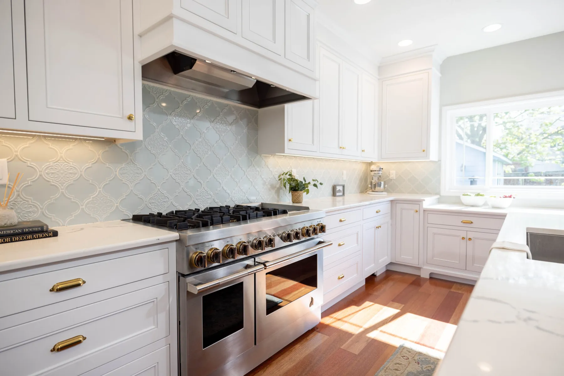 The finished Davis range wall — a professional double range under a custom hood, pale blue arabesque tile and brass hardware on white cabinetry