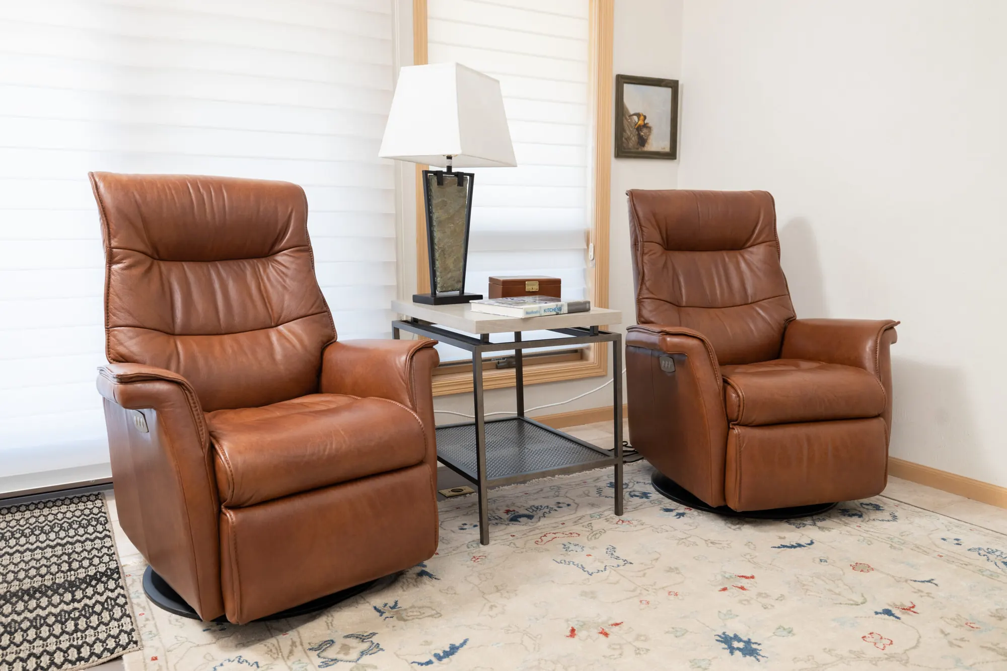 Two leather recliners either side of a small table and lamp, on a patterned rug in a light-walled living room
