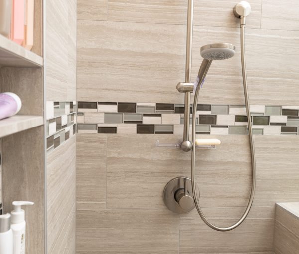 Bathroom shower with neutral wall tile, horizontal mosaic accent tile, chrome showerhead, and built-in shelving.