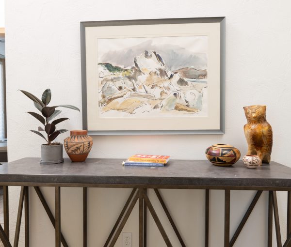 Dining room console table with framed artwork, decorative bowls, pottery, books, and a table lamp.