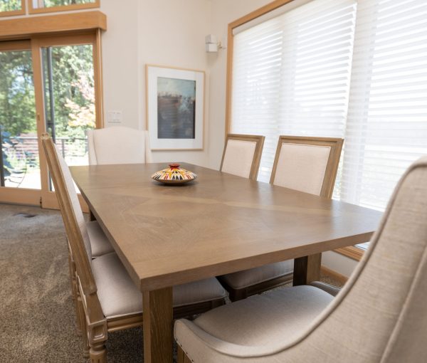 Dining room with rectangular wood table, upholstered dining chairs, white window shades, and framed wall art.