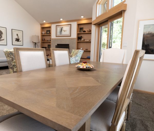 Dining room with warm wood table, upholstered chairs, built-in shelving, fireplace, and large windows.