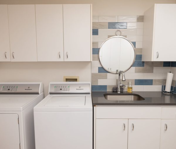 Laundry room with white cabinets, washer and dryer, utility sink, quartz countertop, and white, gray, and blue tile backsplash.