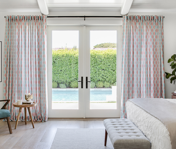 Soft drapery, natural light, and a simple bench create a calm bedroom transition to the outdoors.