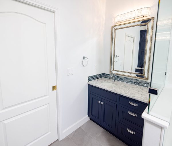 Bathroom vanity with dark blue cabinetry, stone countertop, framed mirror, tile backsplash, and polished hardware.