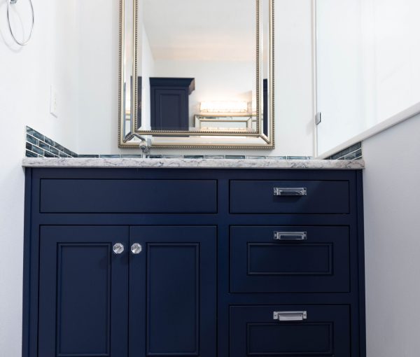 Front view of dark blue bathroom vanity with drawers, cabinet doors, stone countertop, framed mirror, and tile backsplash.