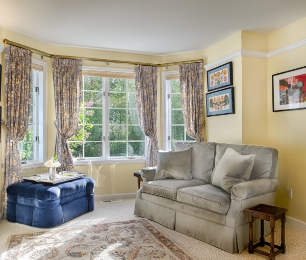 Classic drapery, a blue upholstered ottoman, and collected artwork bring color and personality to this relaxed living room.