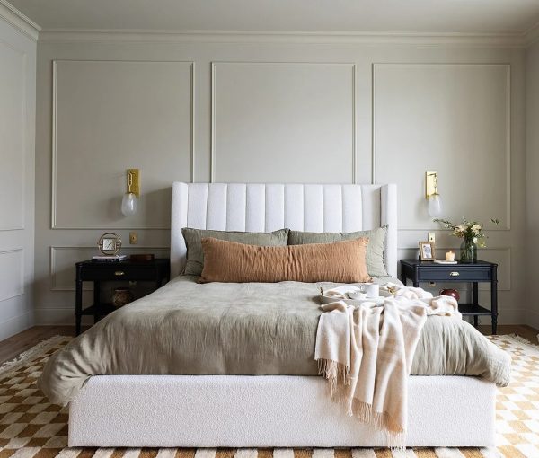 Bedroom with upholstered headboard, white bedding, coral accent pillow, throw blanket, bedside tables, and wall paneling.
