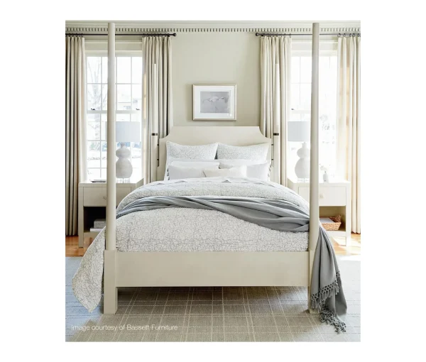 Bedroom with upholstered bed, soft neutral bedding, bedside tables, lamps, windows, and drapery.
