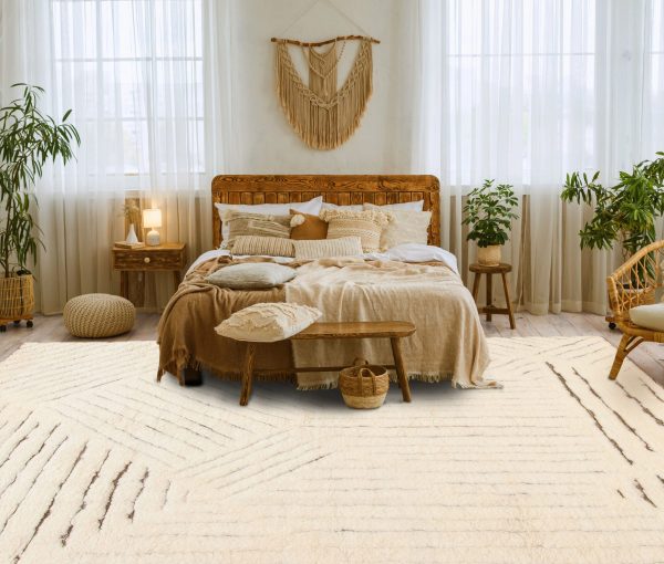 Bohemian bedroom with wood bed frame, neutral bedding, woven wall hanging, plants, and layered area rug.