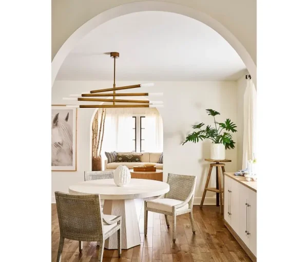 Dining room viewed through an arched doorway with round table, upholstered chairs, warm wood floors, and pendant light.