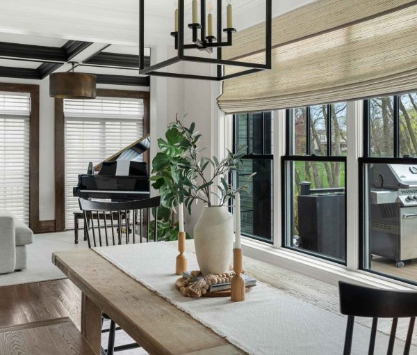 Dining room with wood table, bench seating, black-framed windows, woven light fixture, and plant centerpiece.